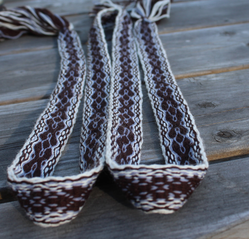Three woven braided straps with a brown, white, and gray pattern, laid out on a weathered gray wooden plank surface.