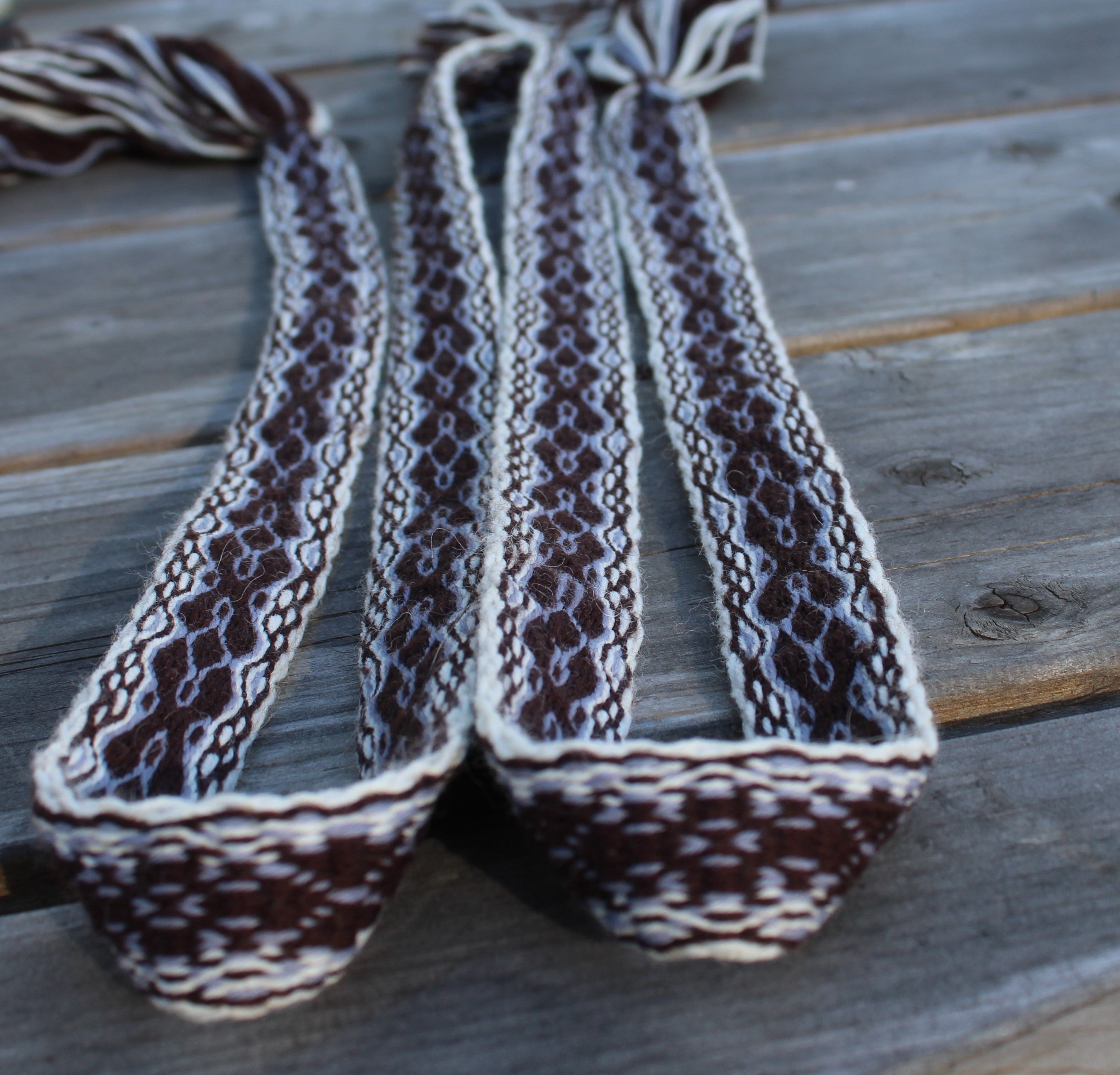 Three woven braided straps with a brown, white, and gray pattern, laid out on a weathered gray wooden plank surface.