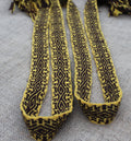A close-up of a woven strap or belt with a black and yellow geometric pattern, laid flat on a textured gray fabric background.