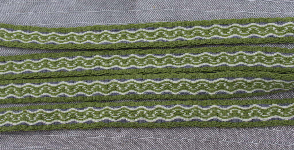 Close-up of olive green patterned ribbon or trim laid horizontally on a gray textured fabric background.