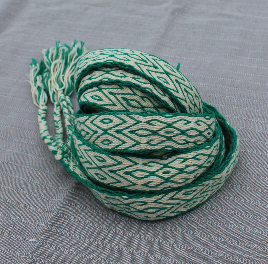 A coiled length of braided cord trim featuring a green and off-white geometric diamond pattern, with frayed ends, displayed on a textured gray fabric background.