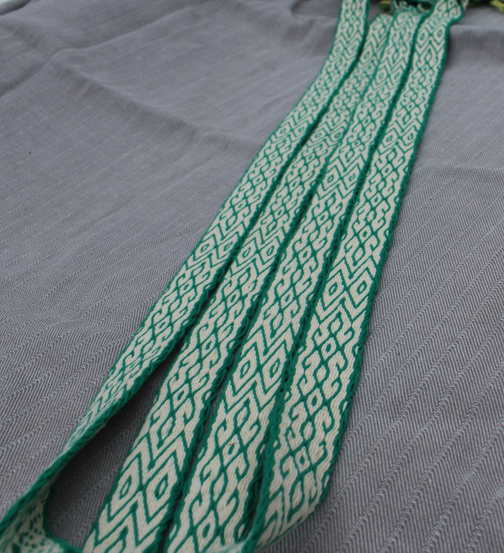 A close-up of a green and white geometric patterned woven strap laid diagonally across a textured gray fabric background.