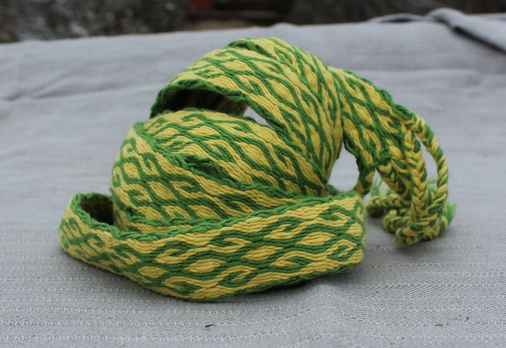 A coiled green and yellow braided rope or cord with a textured woven pattern, resting on a light gray fabric surface.