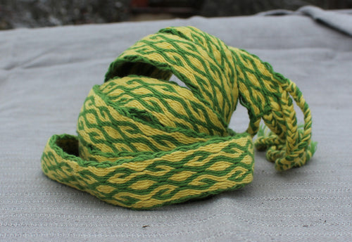 A coiled green and yellow braided rope or cord with a textured woven pattern, resting on a light gray fabric surface.