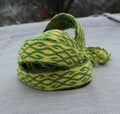 A coiled green and yellow woven strap or cord with a textured wavy pattern, resting on a gray textured fabric surface.