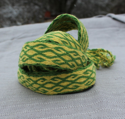 A coiled green and yellow woven strap or cord with a textured wavy pattern, resting on a gray textured fabric surface.