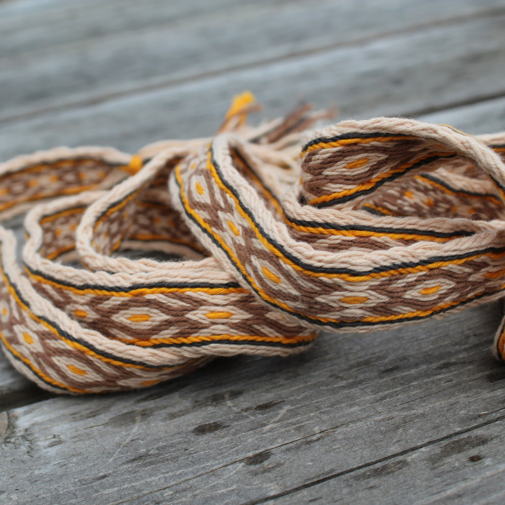 A coiled woven textile with a geometric pattern in brown, beige, and orange, resting on weathered gray wooden planks.