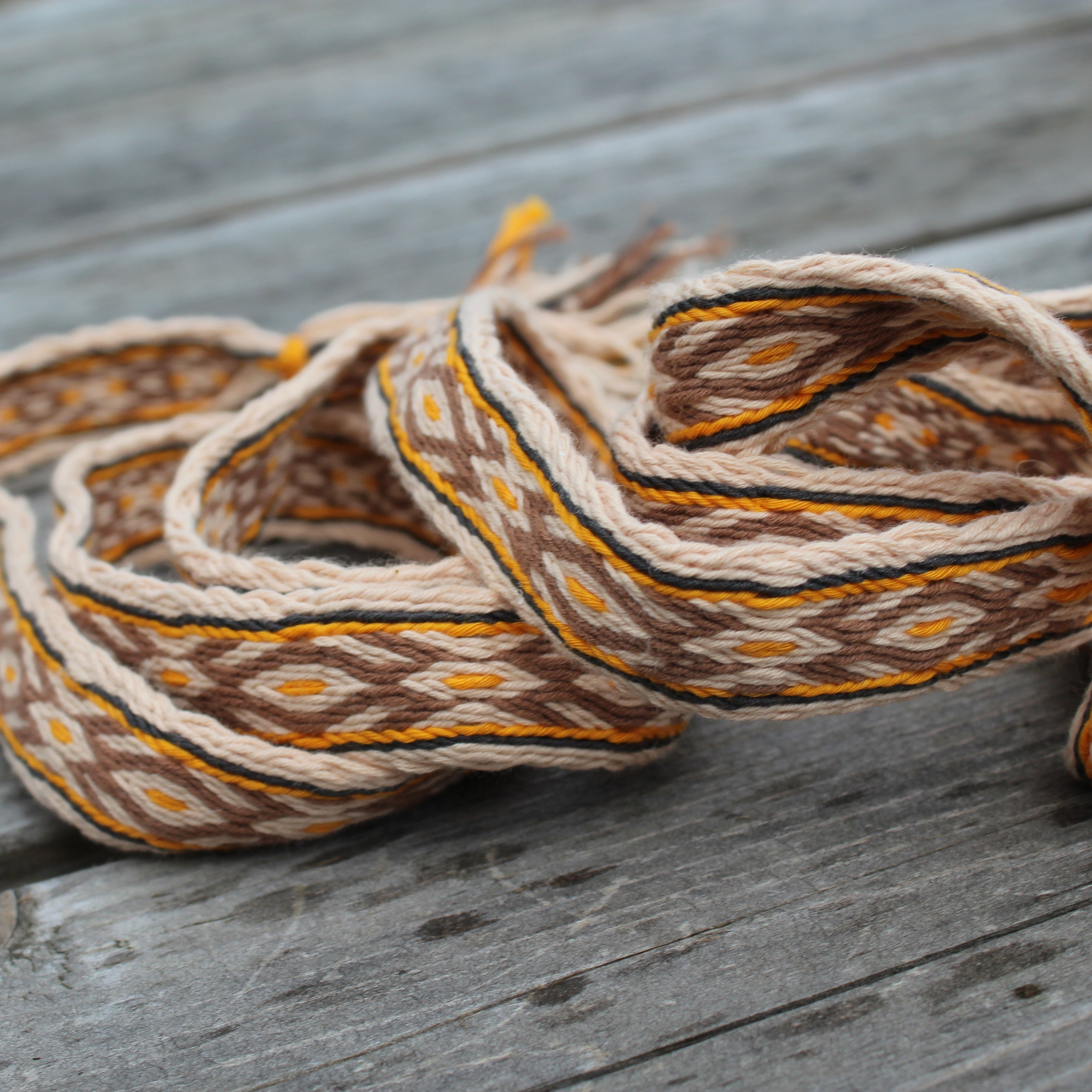 A coiled woven textile with a geometric pattern in brown, beige, and orange, resting on weathered gray wooden planks.