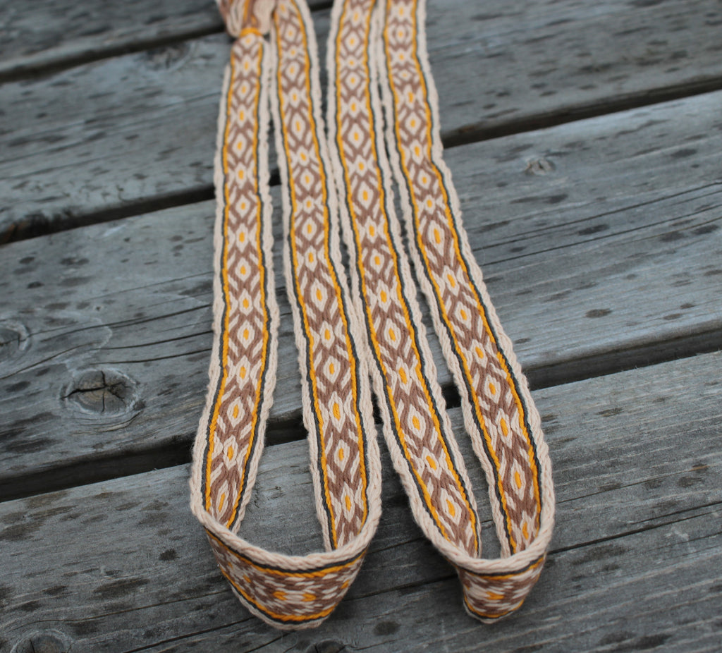A close-up of a braided rope strap with a geometric pattern in beige, brown, and yellow, laid on weathered gray wooden planks.