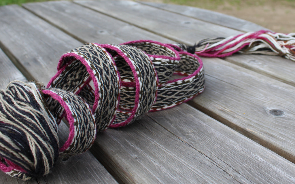 A handmade braided rope garland with pink and black accents, resting on a weathered gray wooden table.