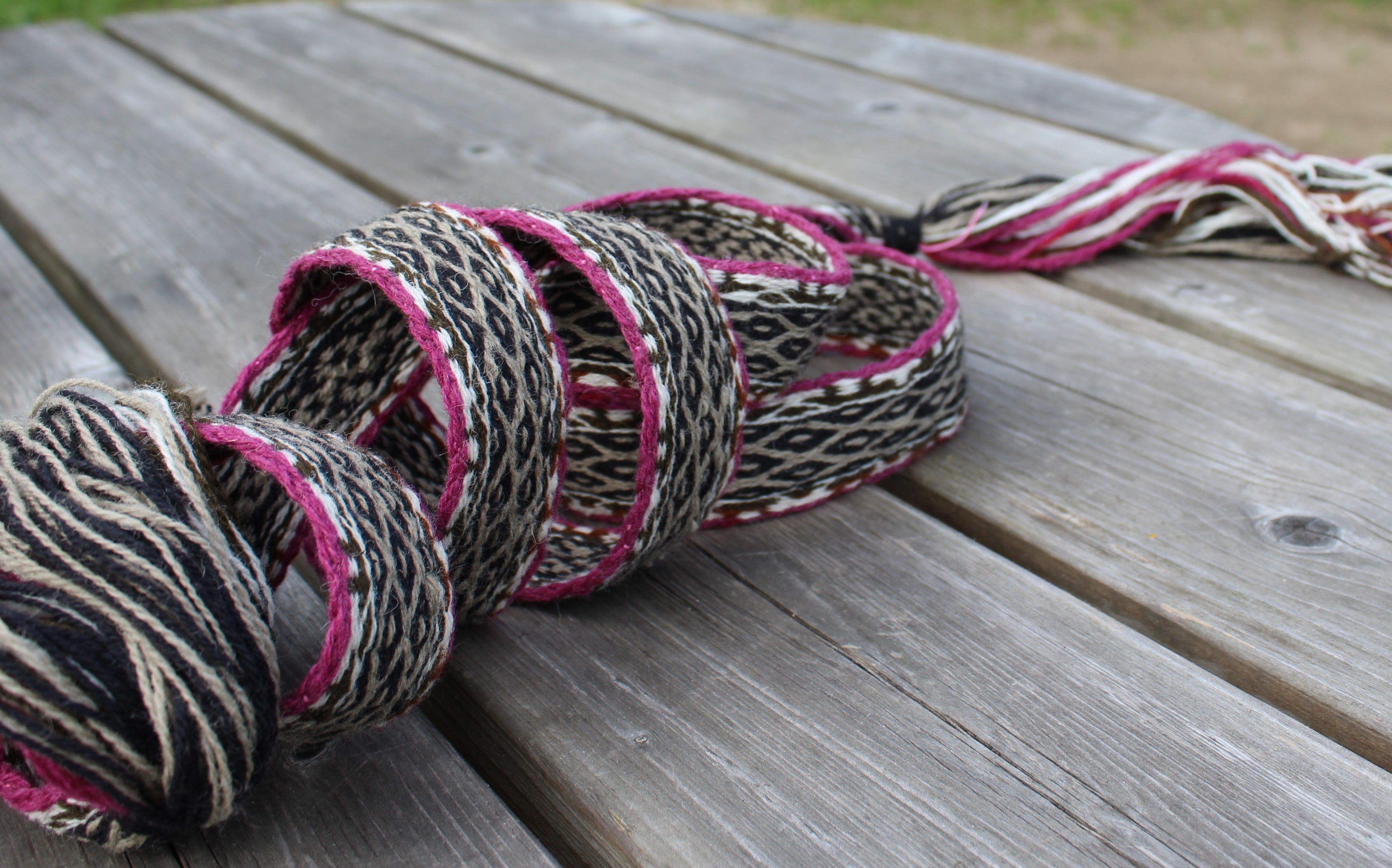 A handmade braided rope garland with pink and black accents, resting on a weathered gray wooden table.