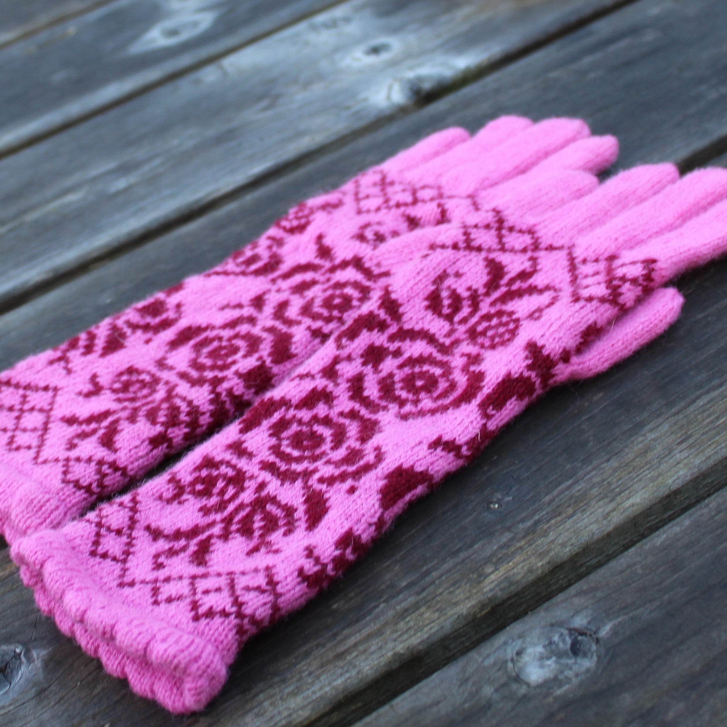 Pair of pink gloves with a red pattern on a wooden surface