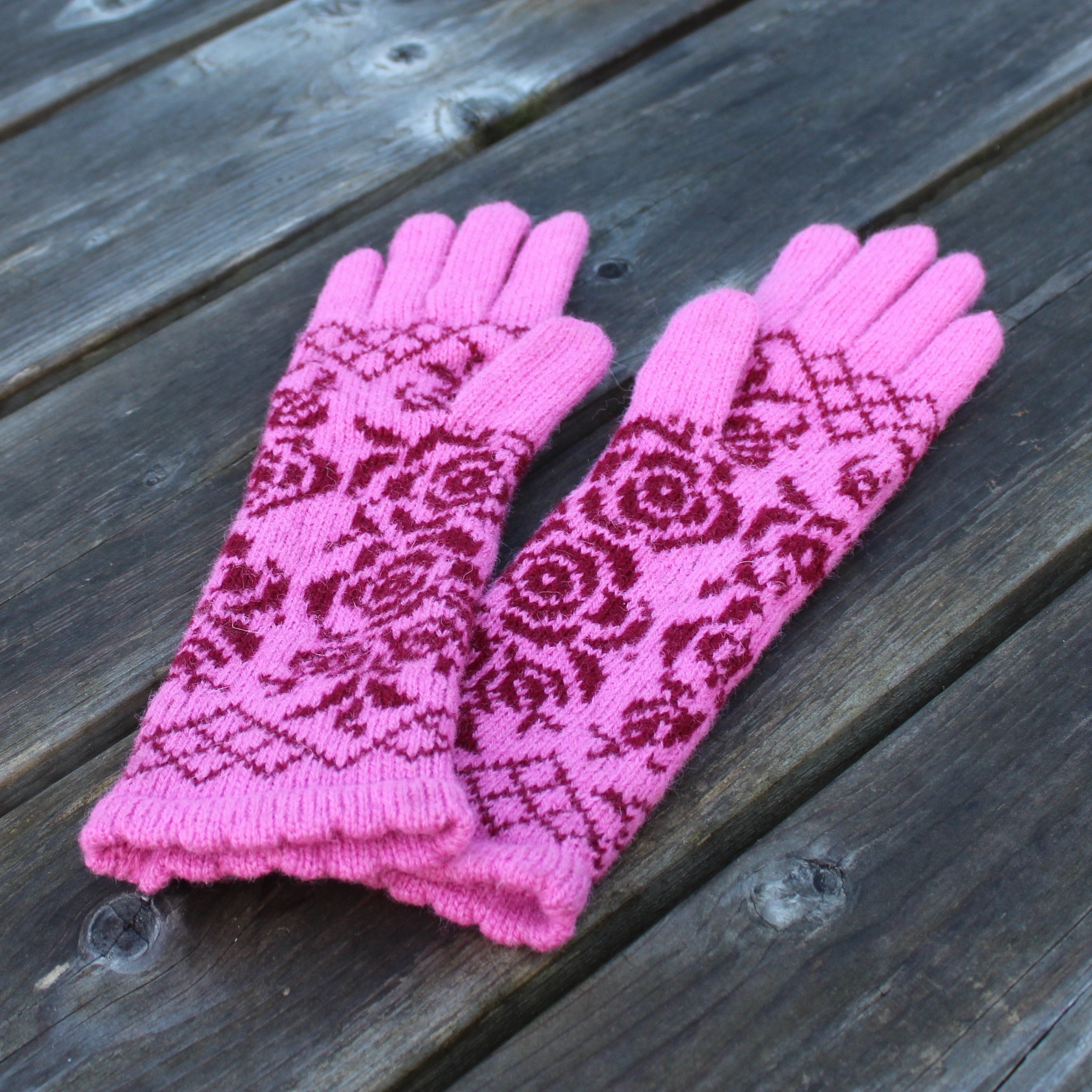 Pair of pink gloves with a red pattern on a wooden surface