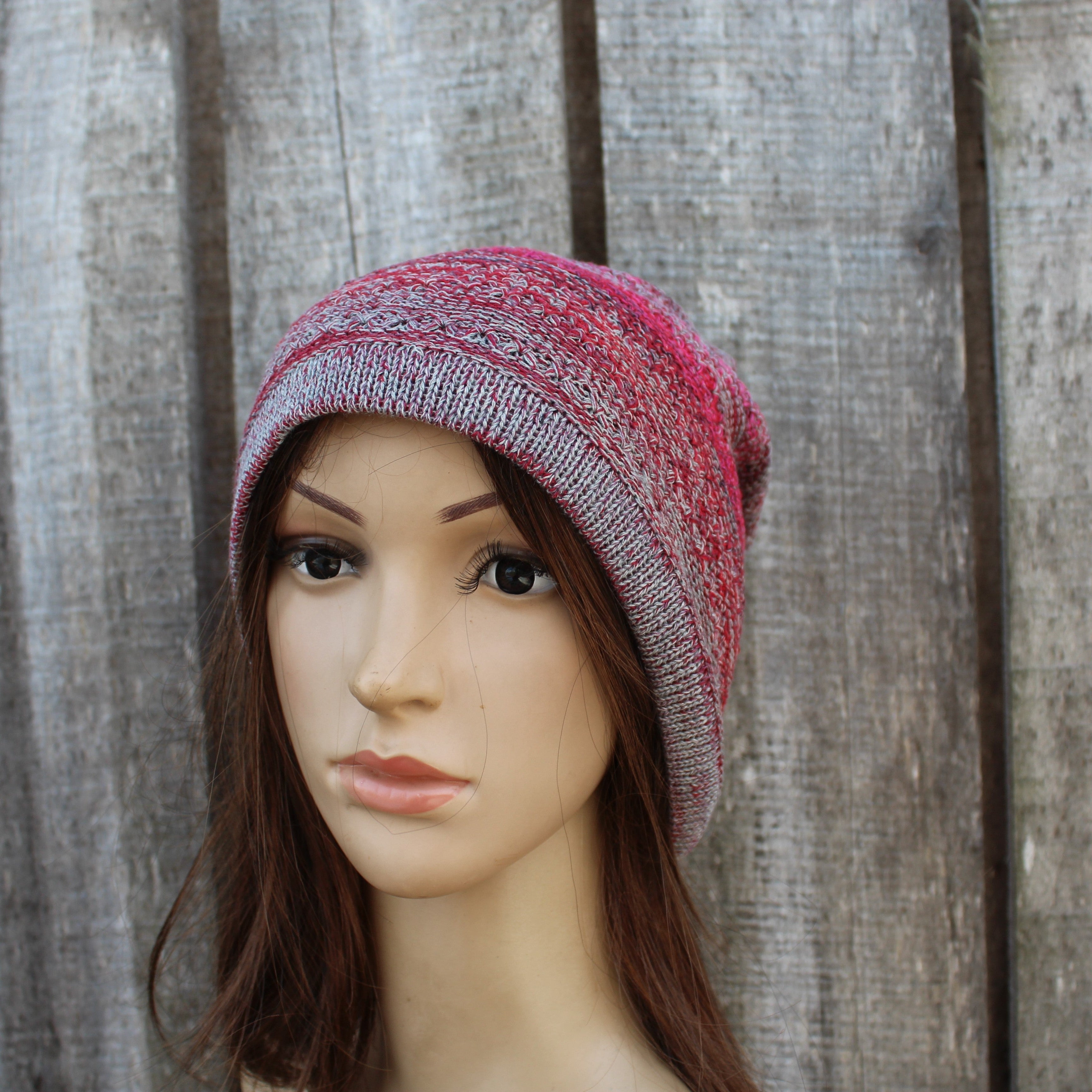 Mannequin head wearing a pink and gray knit beanie against a wooden background
