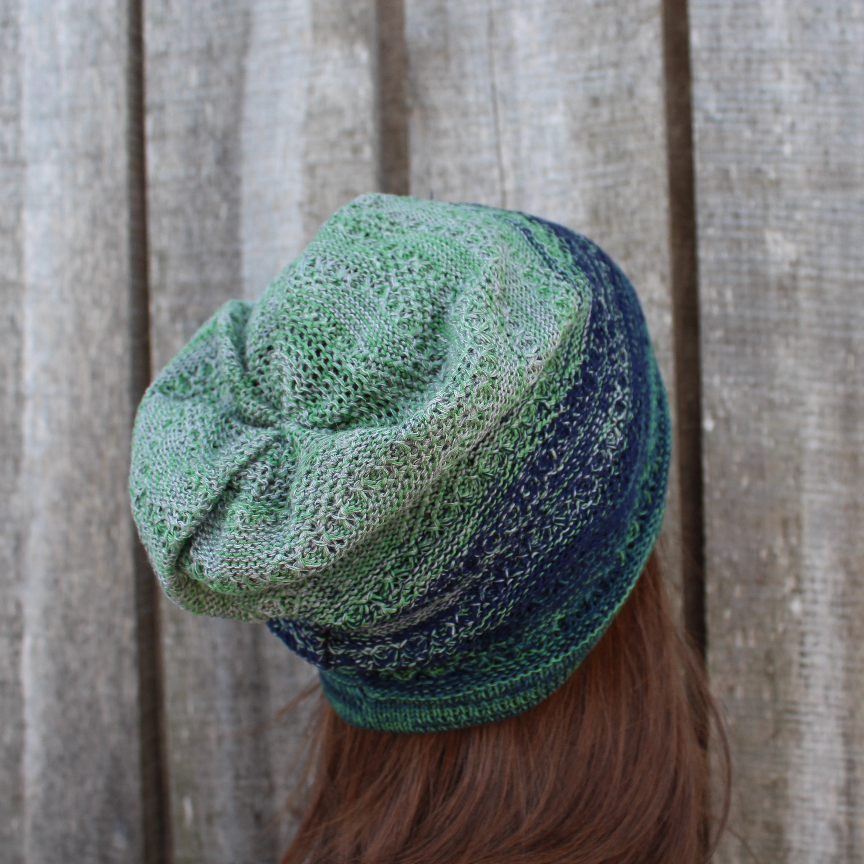 Green and blue knitted hat worn by a person against a wooden background