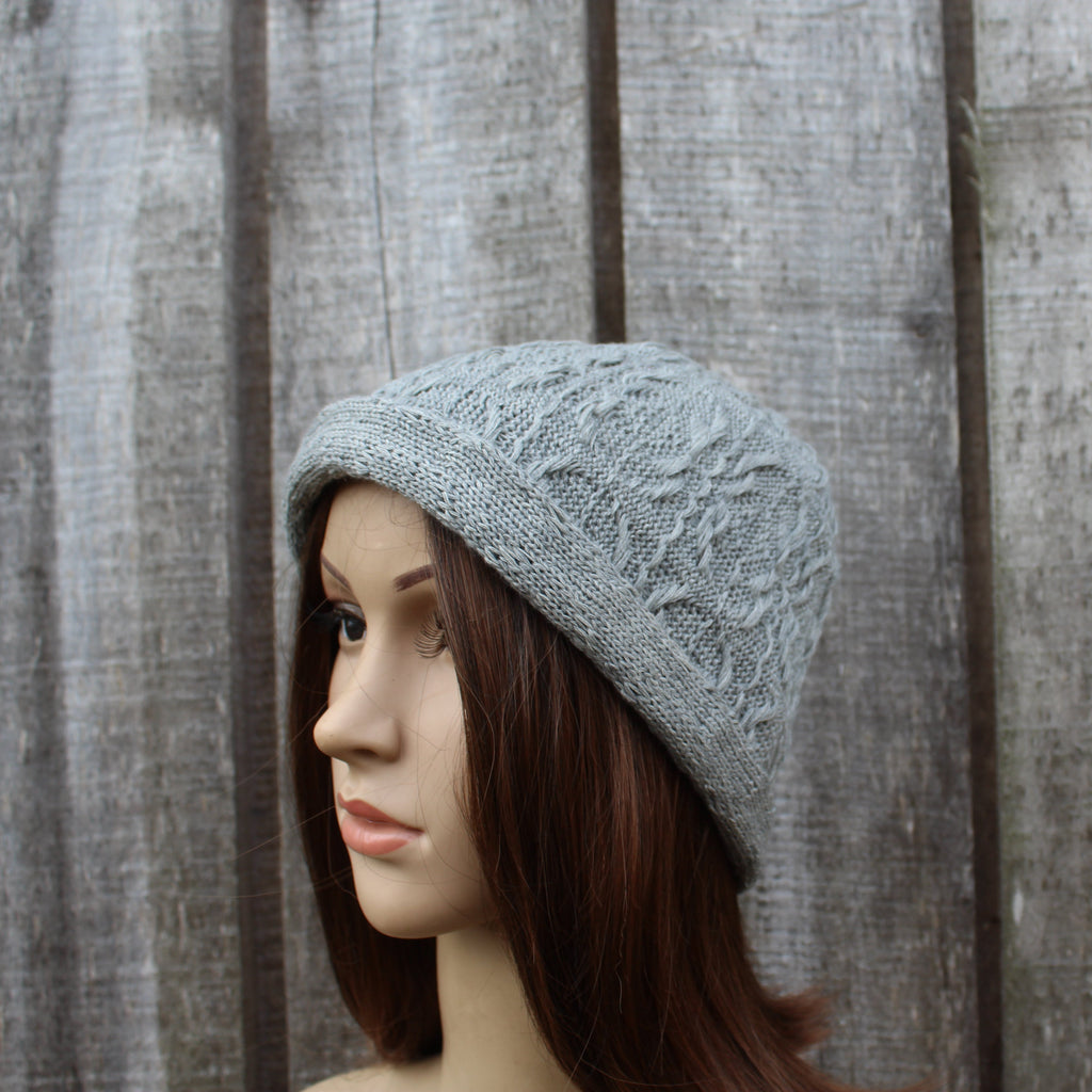 Mannequin head wearing a gray knit beanie against a wooden fence background