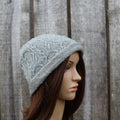 Mannequin head wearing a gray knitted hat against a wooden background