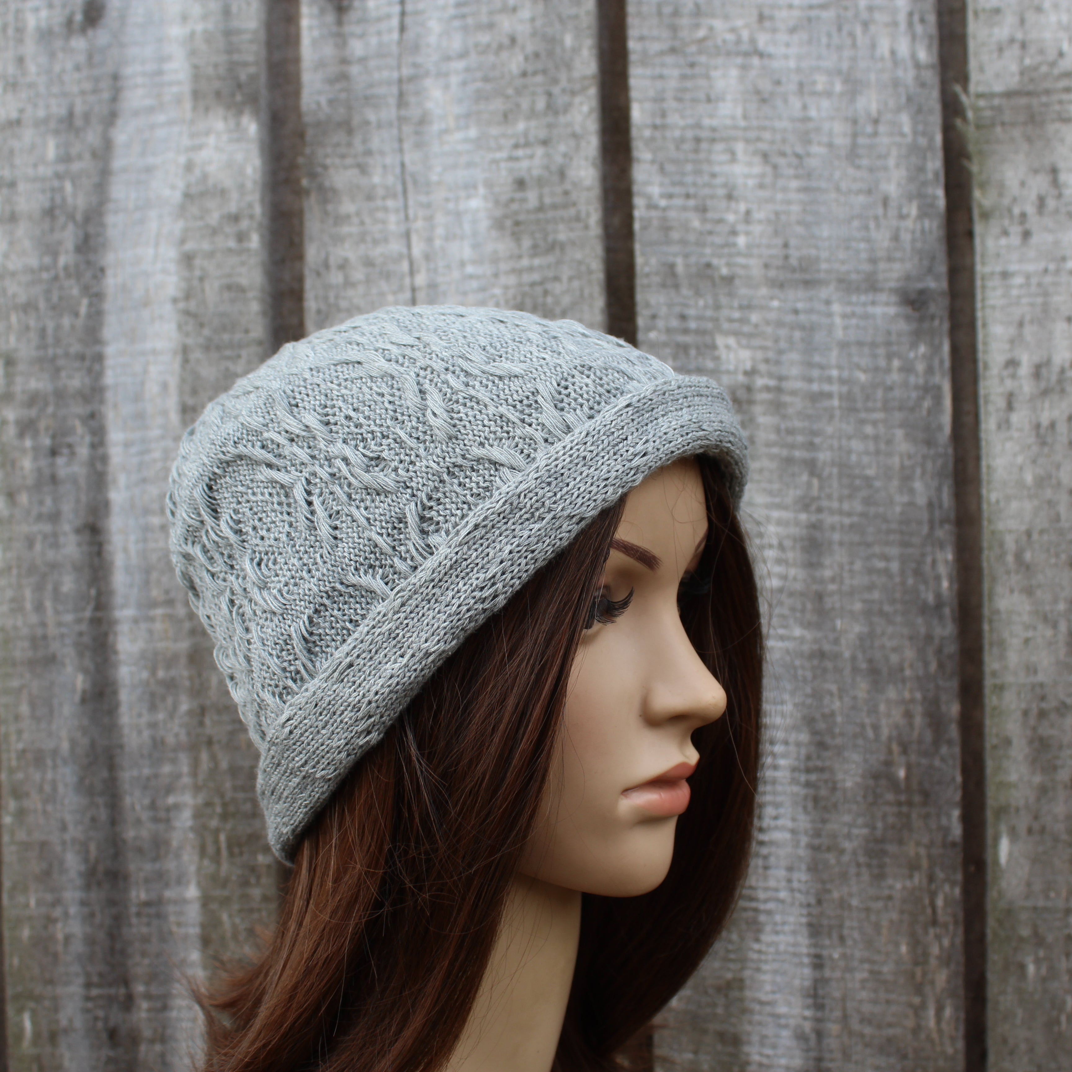 Mannequin head wearing a gray knitted hat against a wooden background