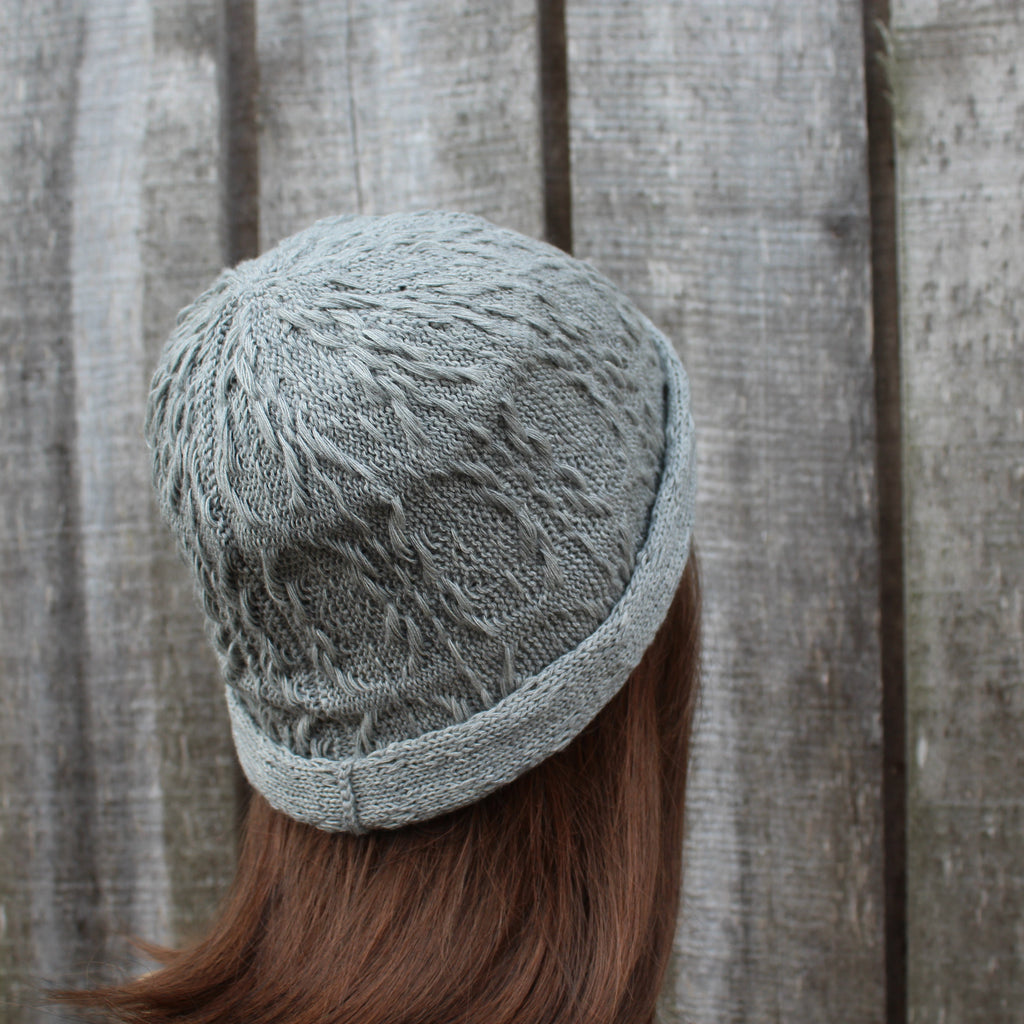 Person wearing a textured gray knit hat against a wooden fence background
