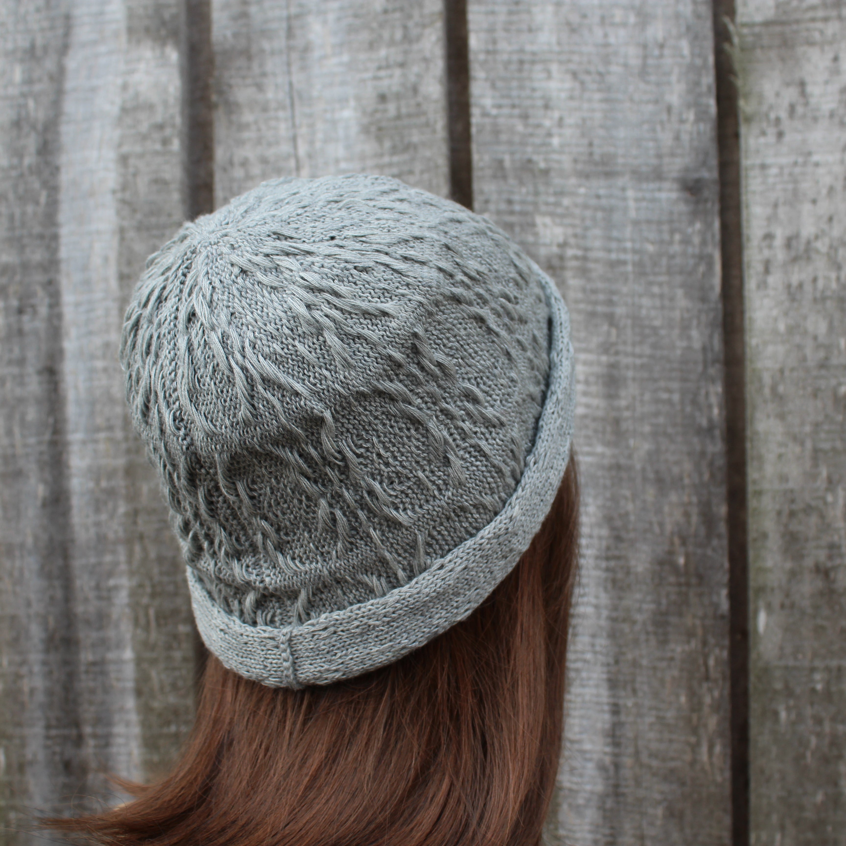 Person wearing a textured gray knit hat against a wooden fence background
