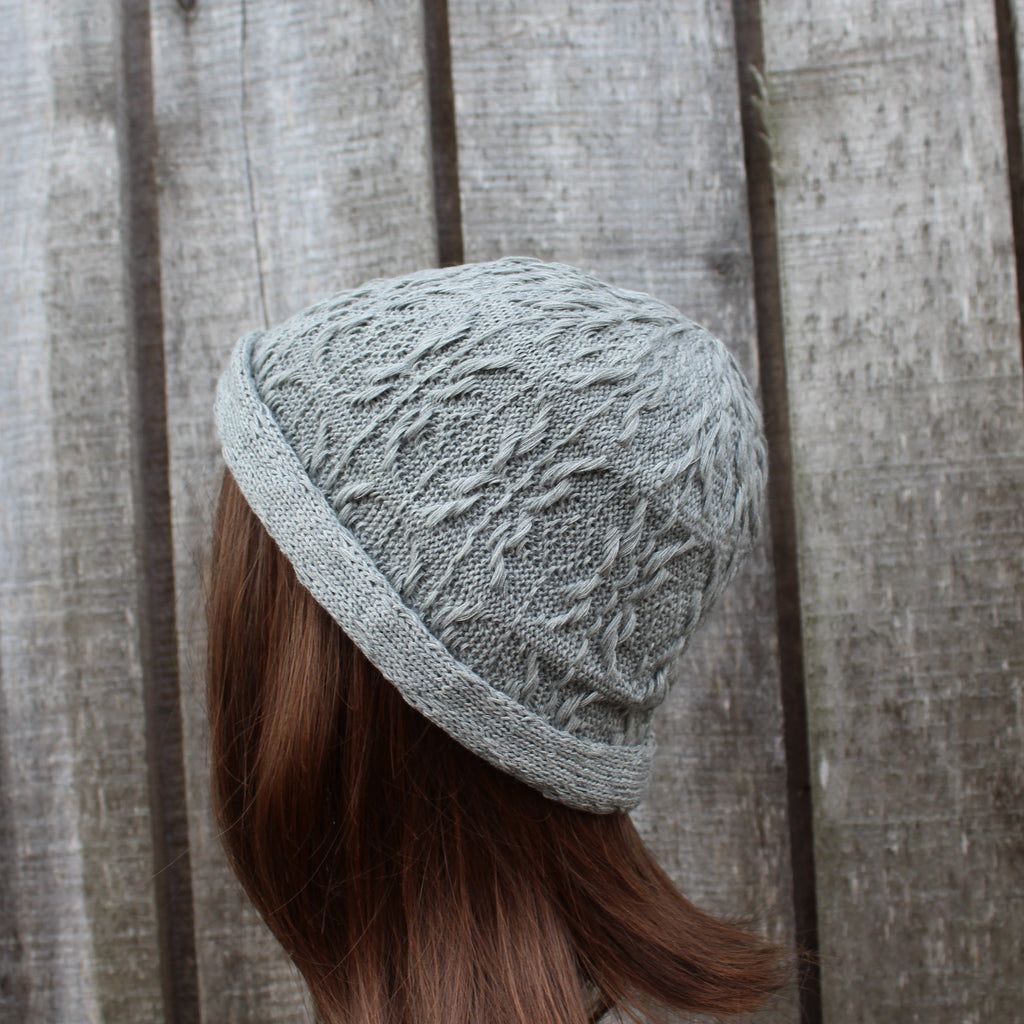 Person wearing a textured gray knit hat against a wooden background