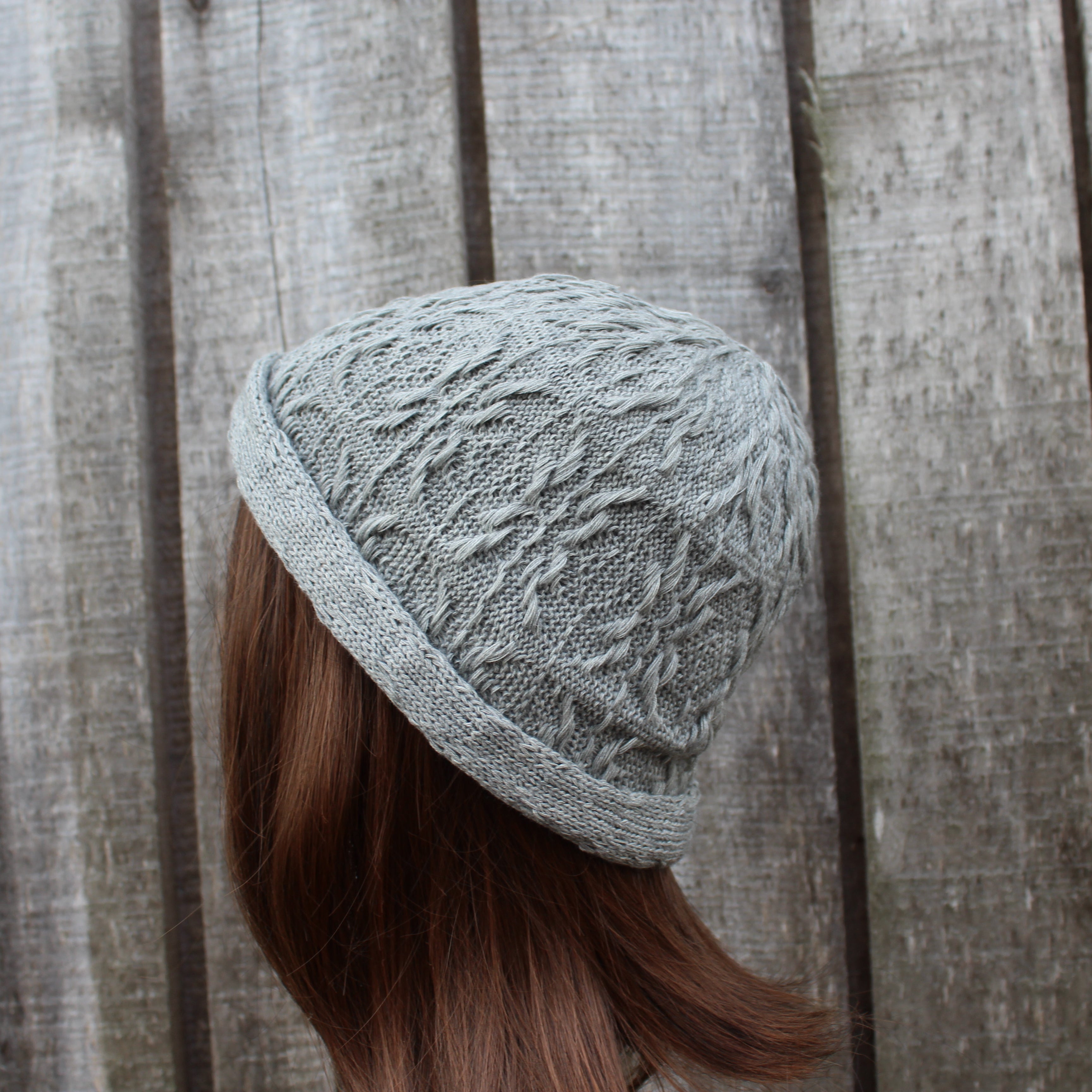 Person wearing a textured gray knit hat against a wooden background