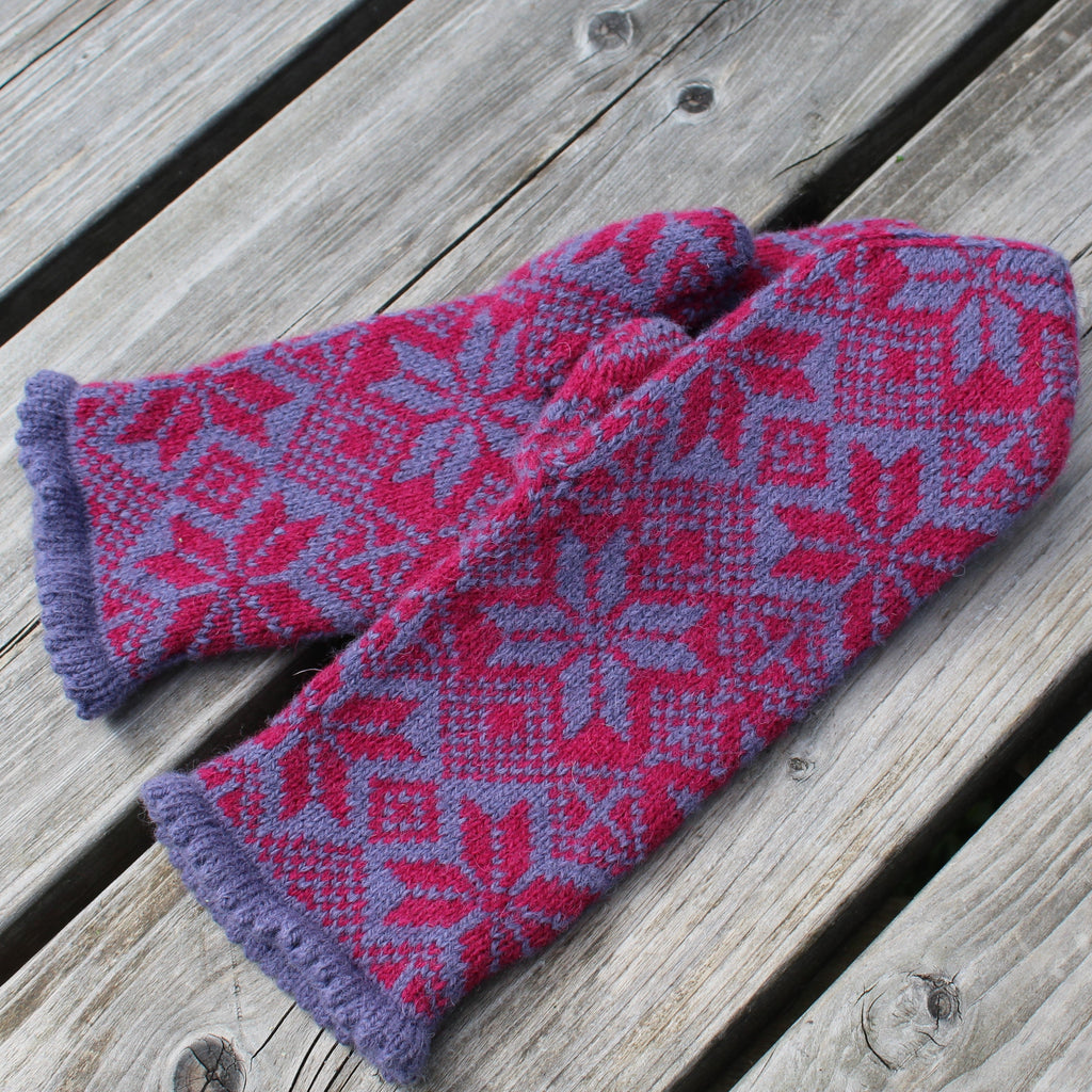Pair of pink and purple patterned mittens on a wooden surface