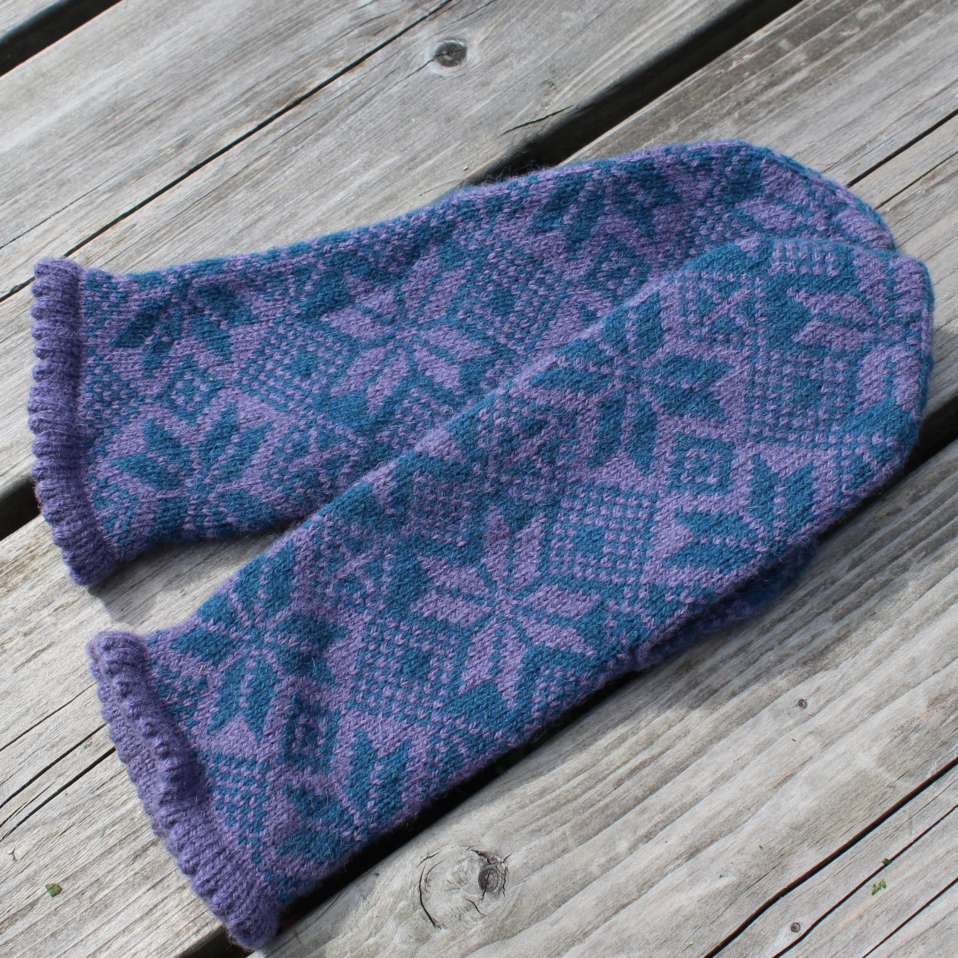 Pair of purple and blue patterned mittens on a wooden surface