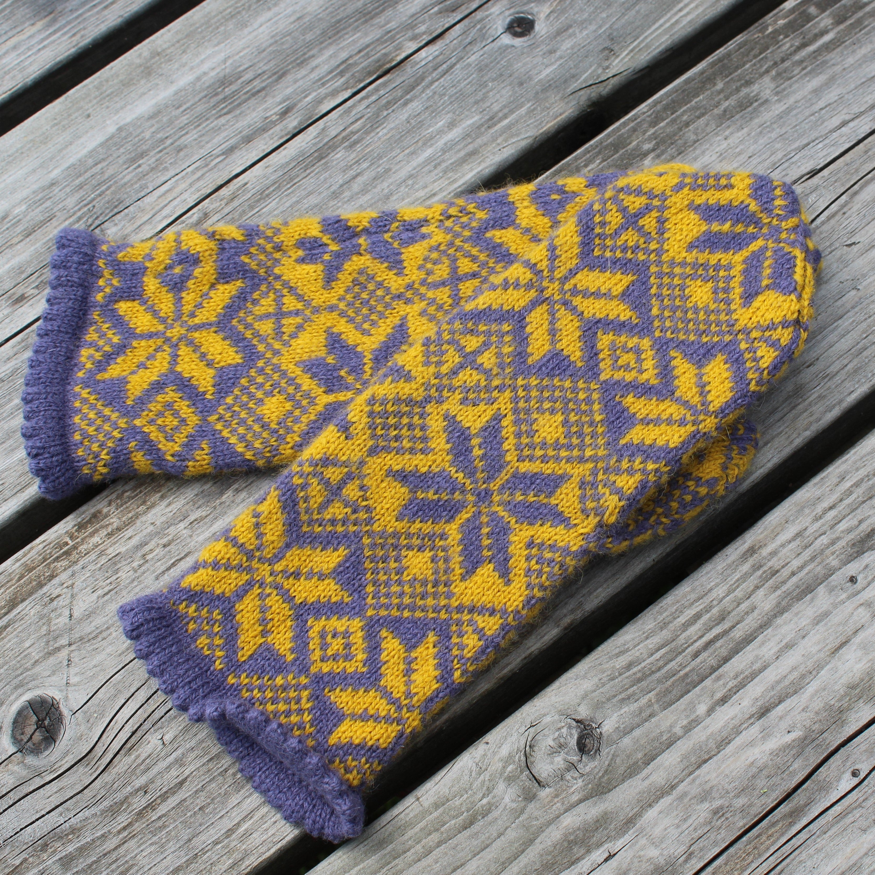Knitted mittens with purple and yellow pattern on a wooden surface