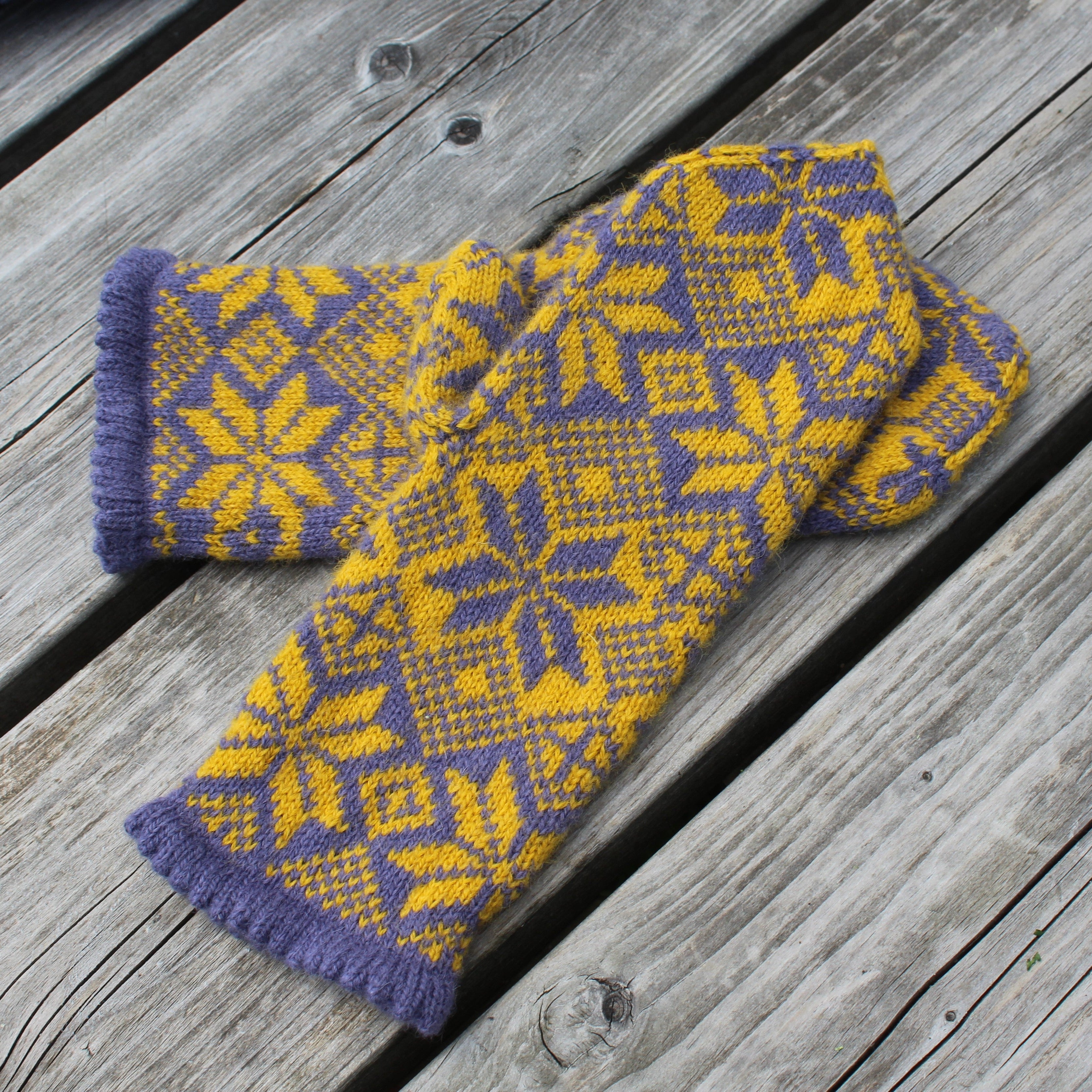 Pair of blue and yellow patterned mittens on a wooden surface