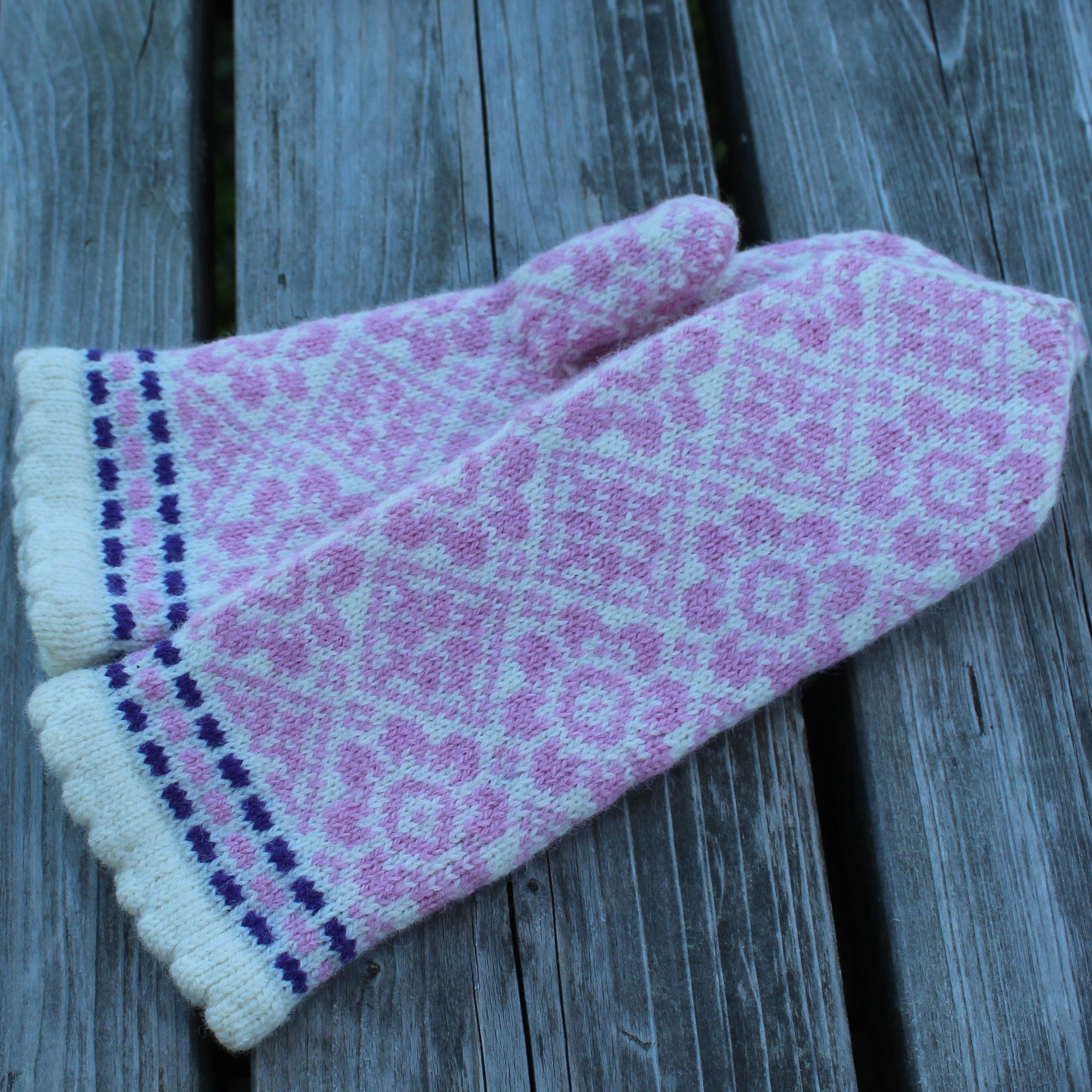Pair of pink knitted mittens with a pattern on a wooden surface