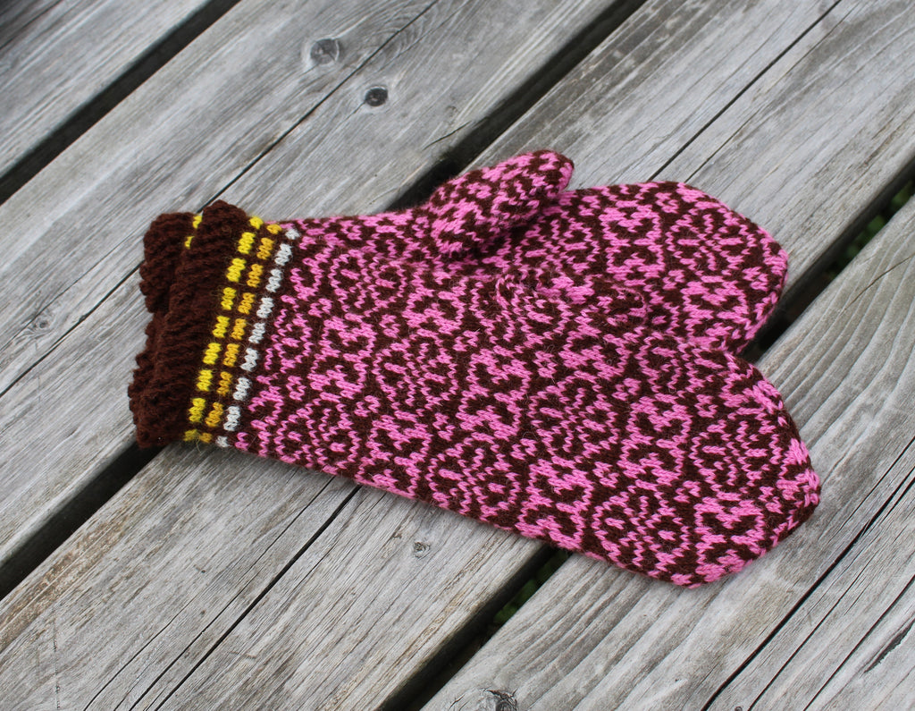 Pair of pink patterned mittens on a wooden surface