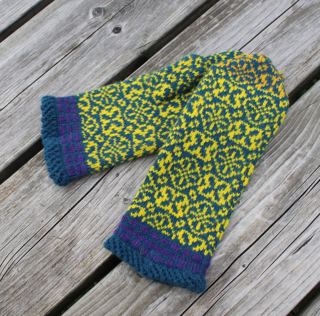 Knitted mittens with a green and yellow pattern on a wooden surface