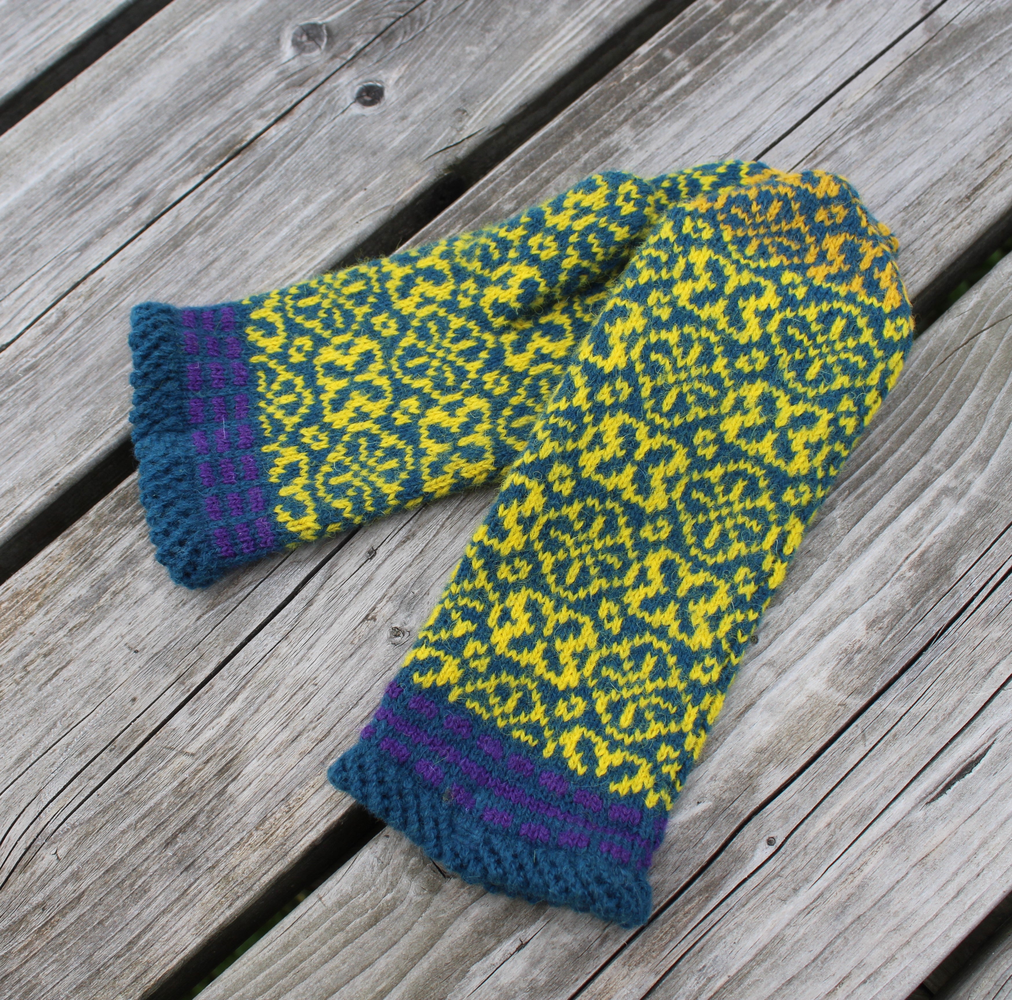 Knitted mittens with a green and yellow pattern on a wooden surface