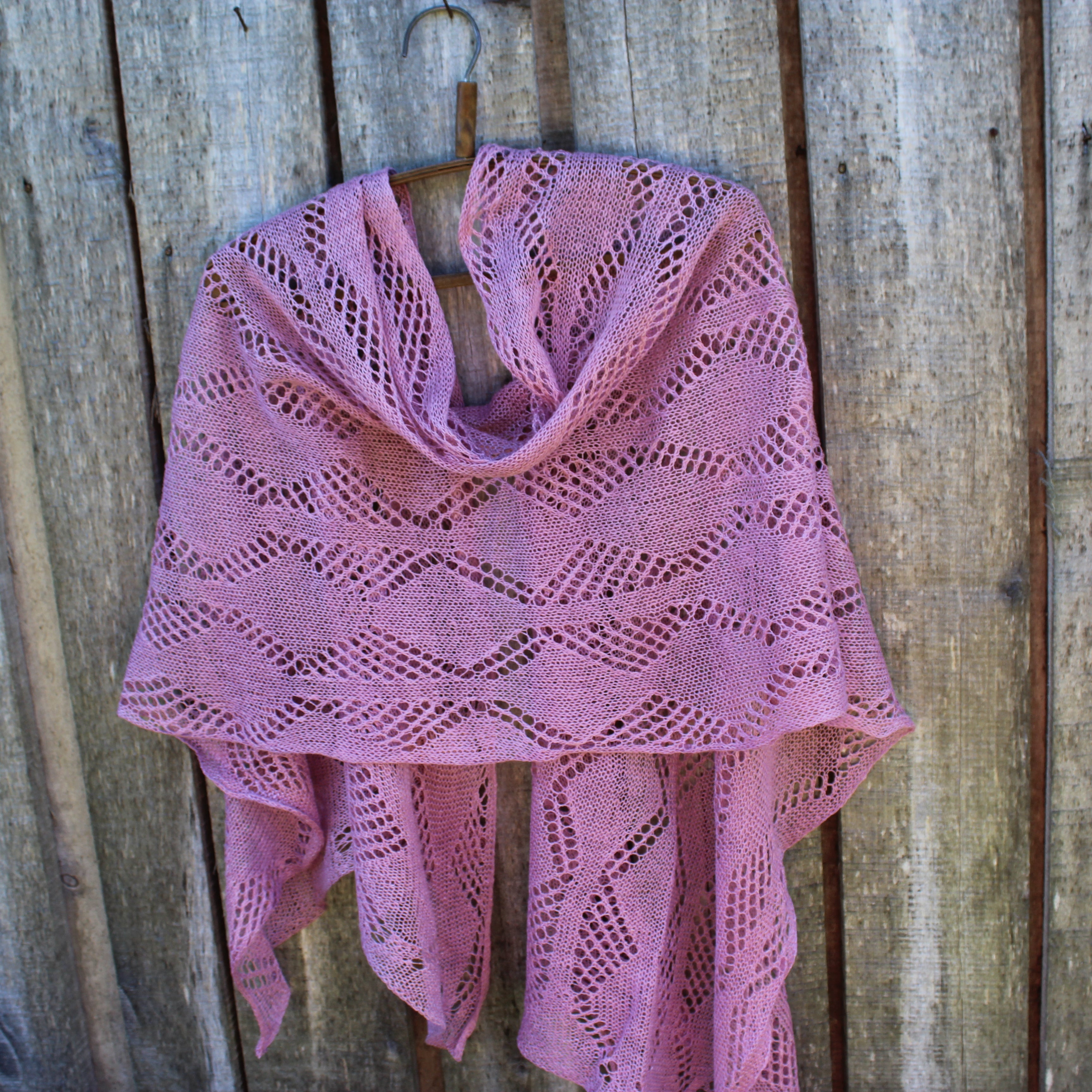 Pink knitted shawl on a wooden hook against a wooden background