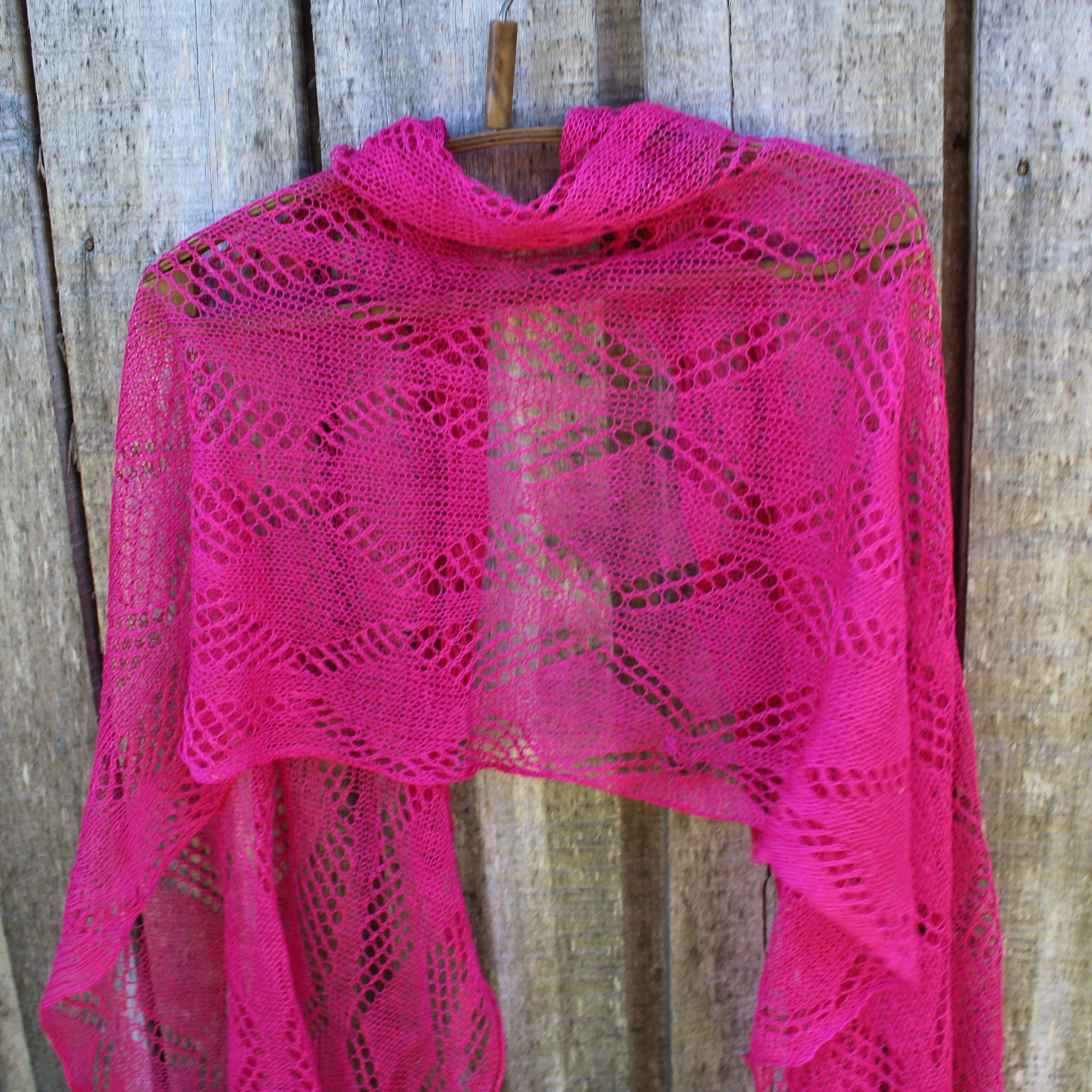 Pink knitted shawl on a wooden hanger against a rustic wooden background