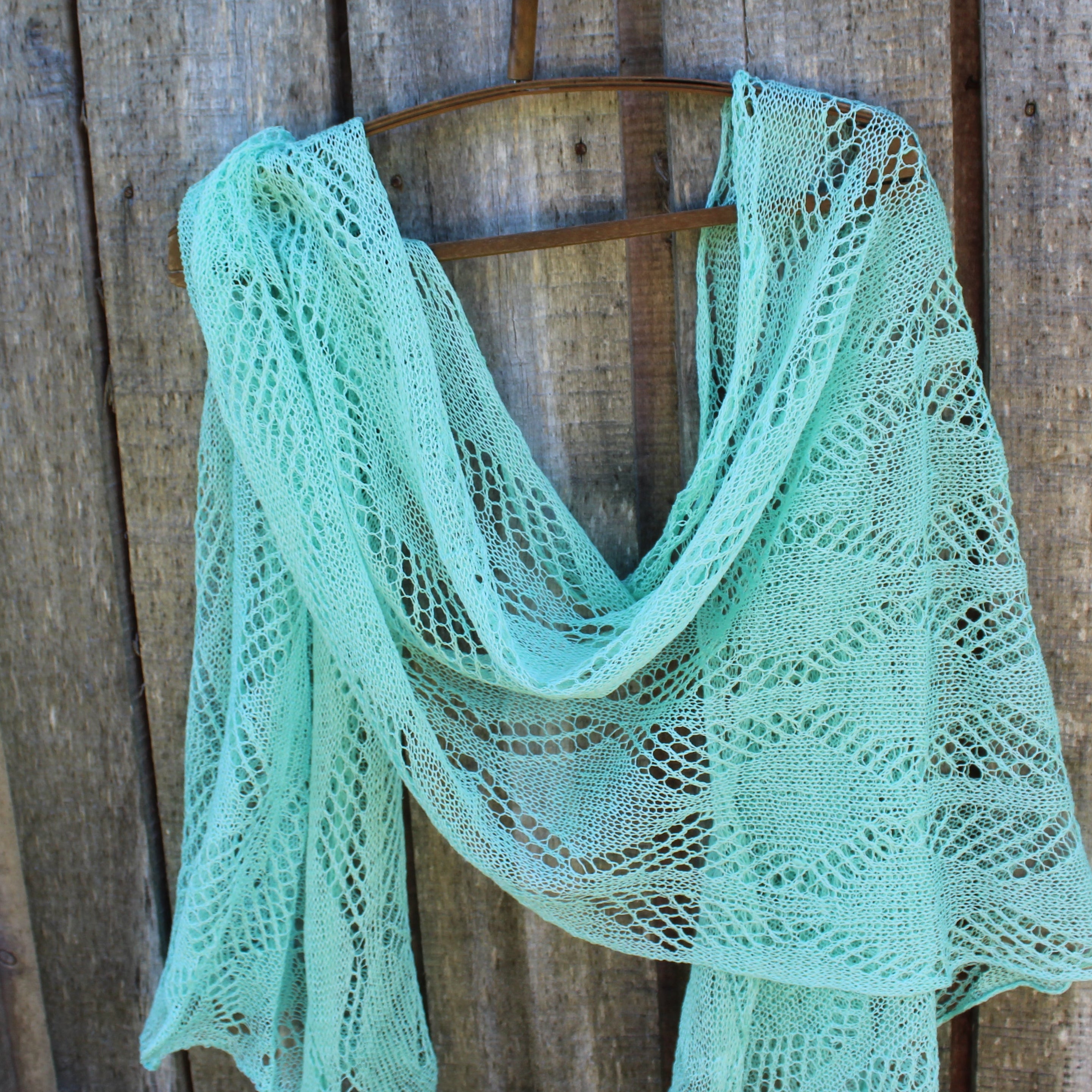 Mint green knitted shawl on a wooden hanger against a rustic wooden background