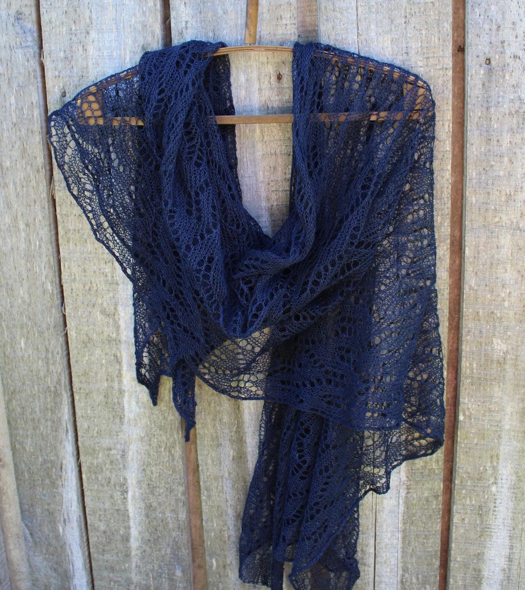 A navy blue open-knit lace shawl draped over a wooden hanger against a rustic light wood plank background.