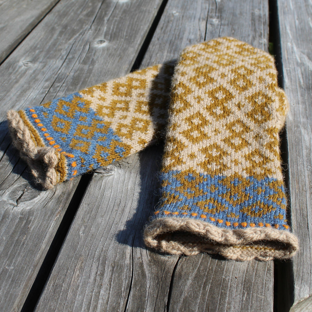 A pair of hand-knit wool mittens with a geometric pattern in mustard yellow, cream, and light blue, laid out on weathered gray wooden planks.