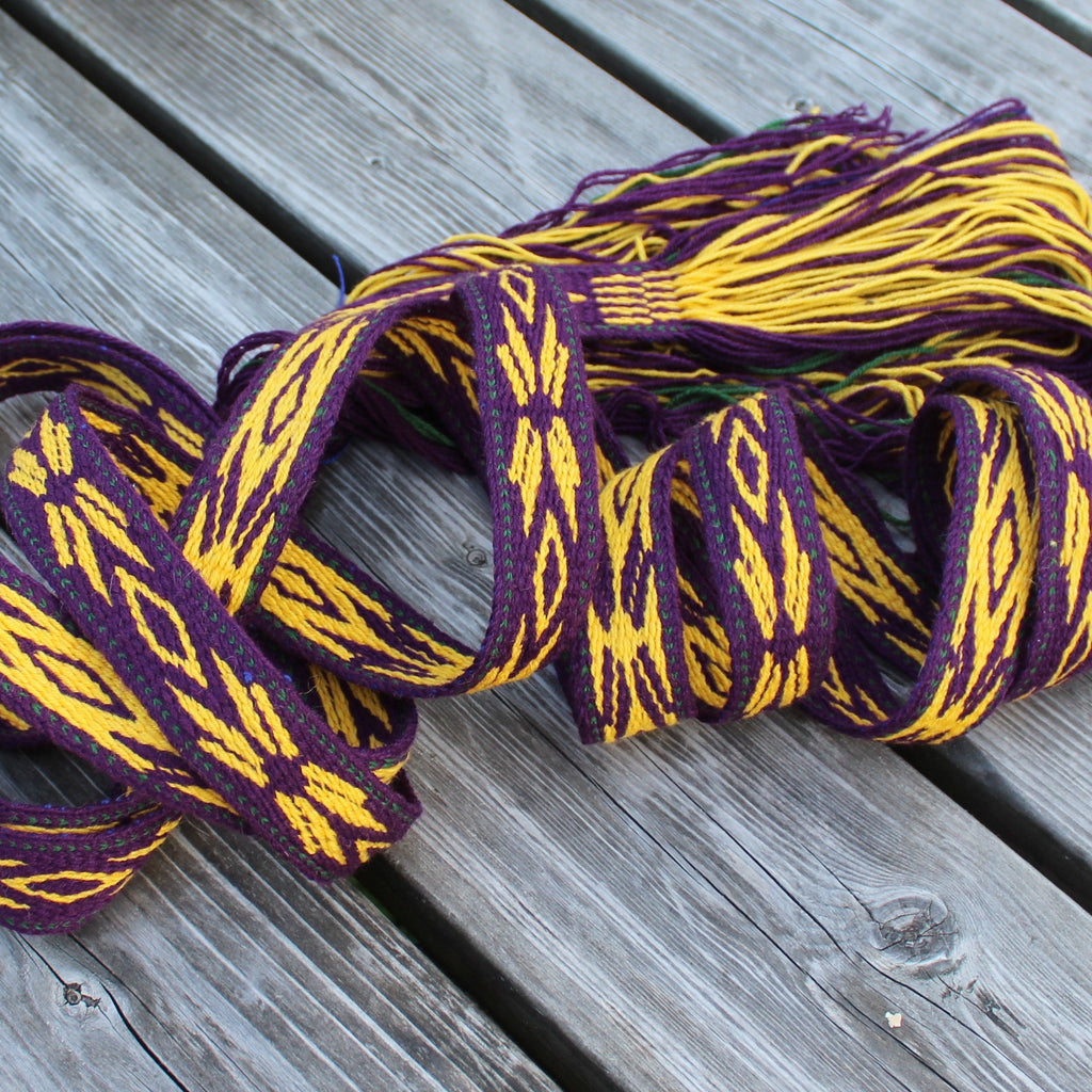 A thick woven scarf with a purple and yellow ikat pattern, coiled on a gray wooden deck.