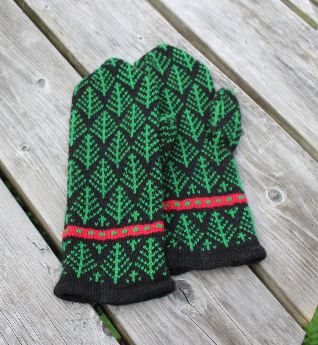 A pair of knit winter gloves with a green and black tree pattern and red accents, laid flat on a weathered gray wooden plank surface.