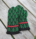 A pair of knit winter gloves with a green and black tree pattern and red accents, laid flat on a weathered gray wooden plank surface.