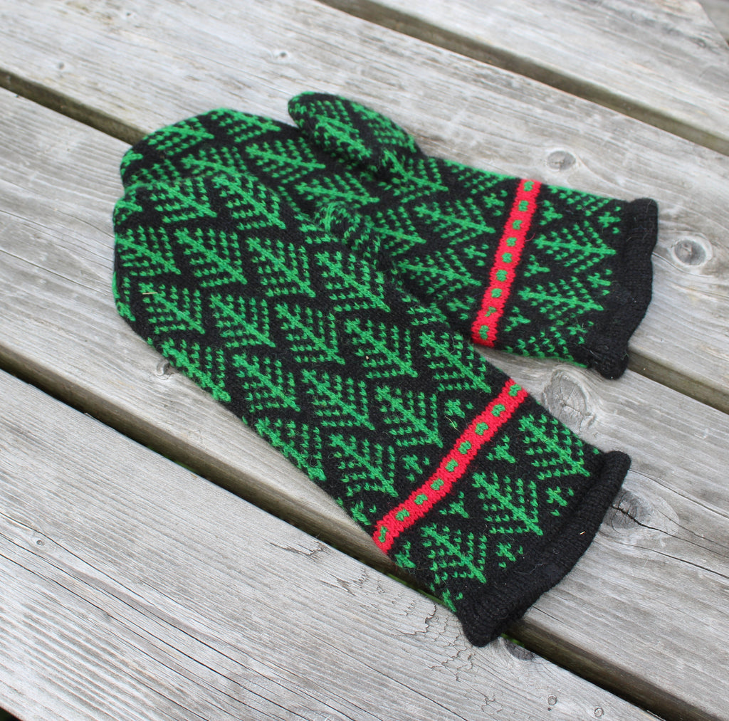 A pair of knit winter mittens with a green and black geometric pattern and red accents, displayed on a weathered gray wooden plank surface.