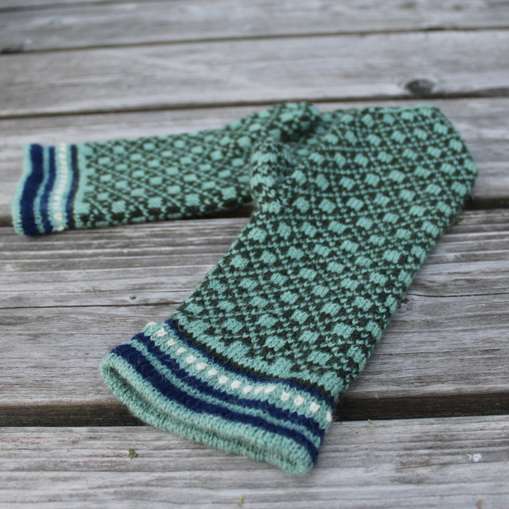 A pair of green and navy blue patterned knit boot covers resting on a weathered gray wooden plank surface.