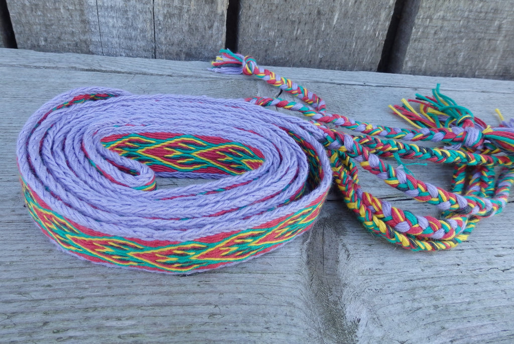 A coiled light purple rope with braided multicolor accents in red, green, yellow, and blue, resting on a weathered gray wooden surface.