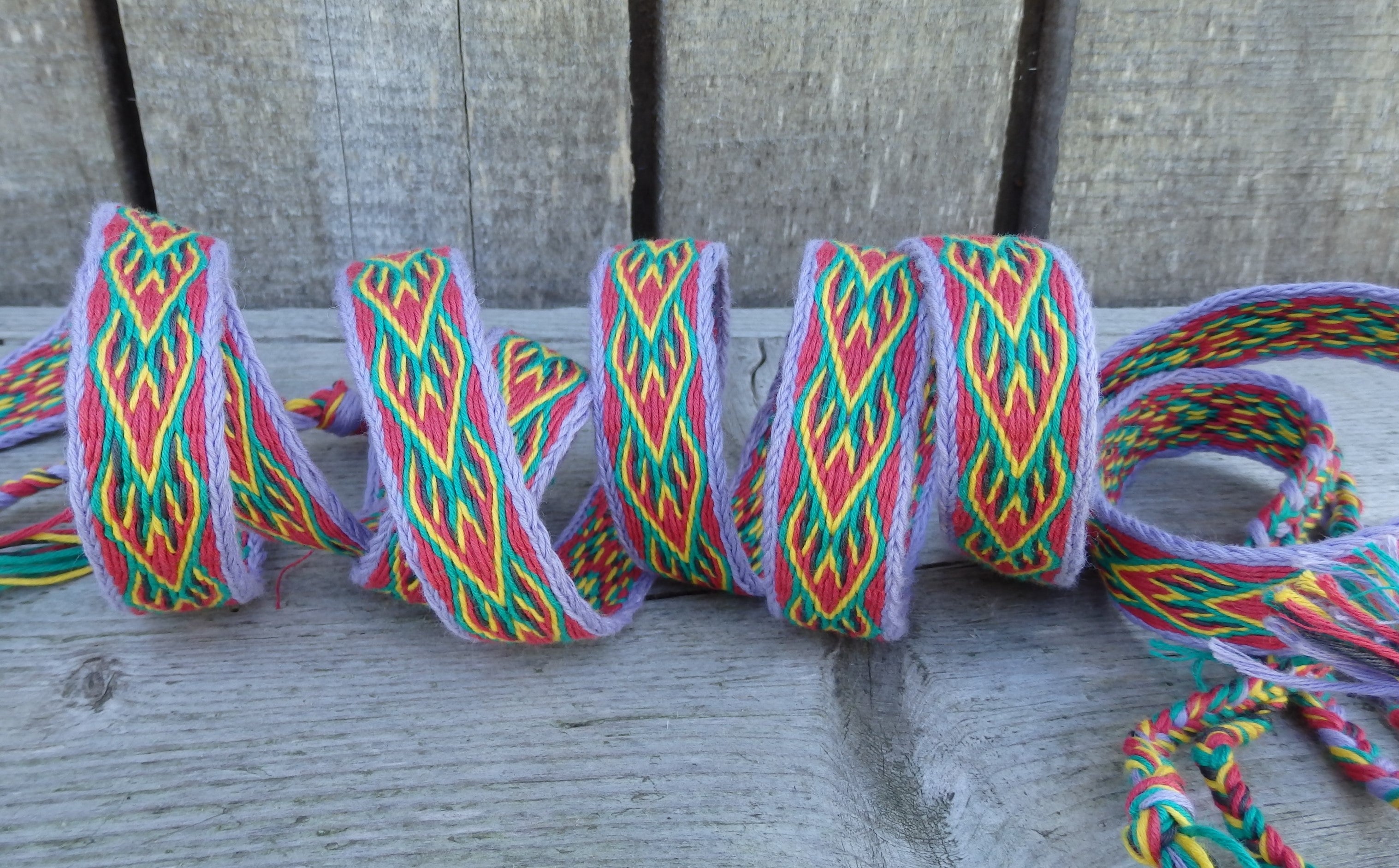 A roll of colorful braided cord trim with a geometric pattern in red, green, yellow, and purple, coiled on a weathered gray wooden surface.
