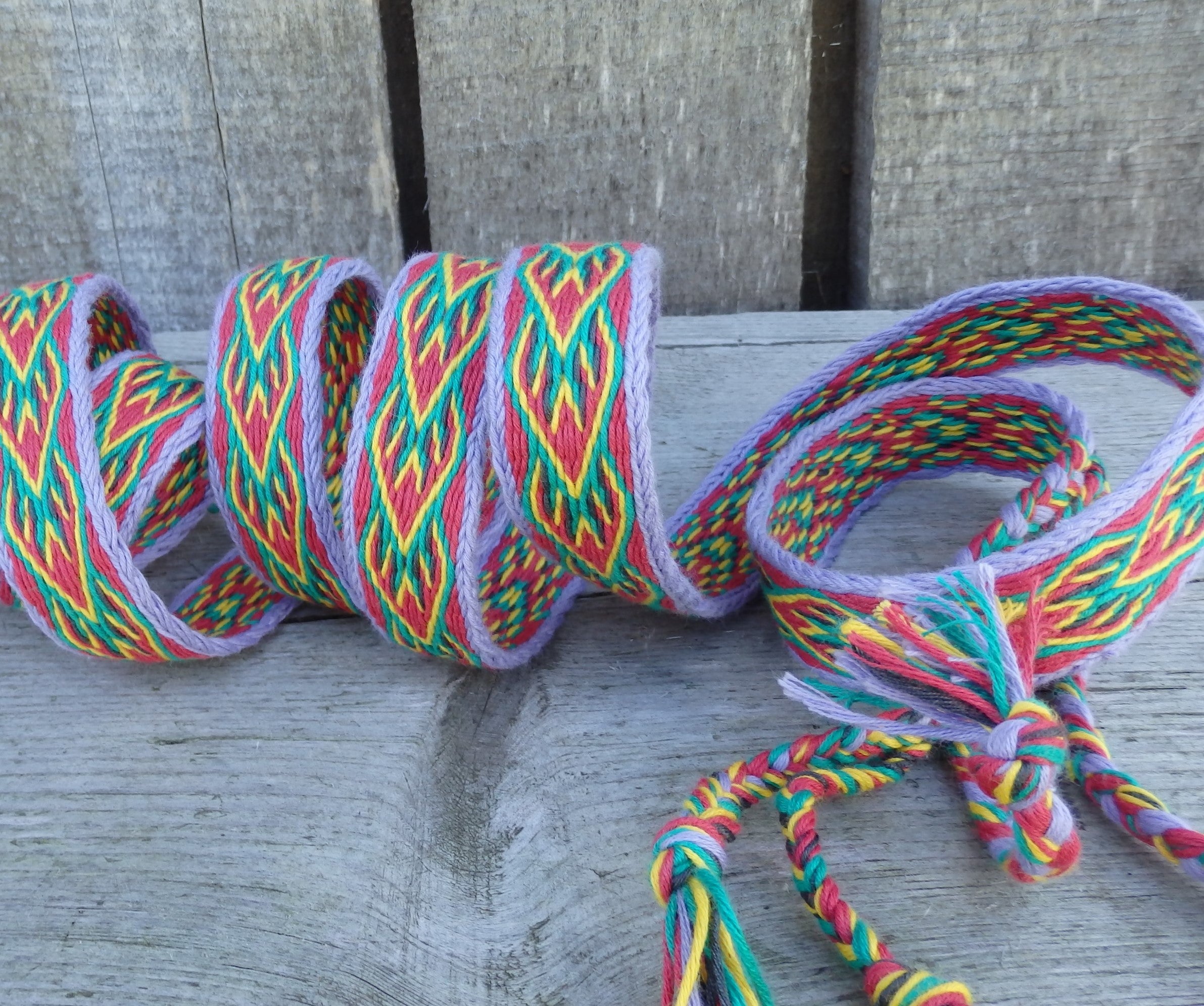 A multicolored braided elastic strap with a geometric pattern, shown coiled on a weathered gray wooden surface.