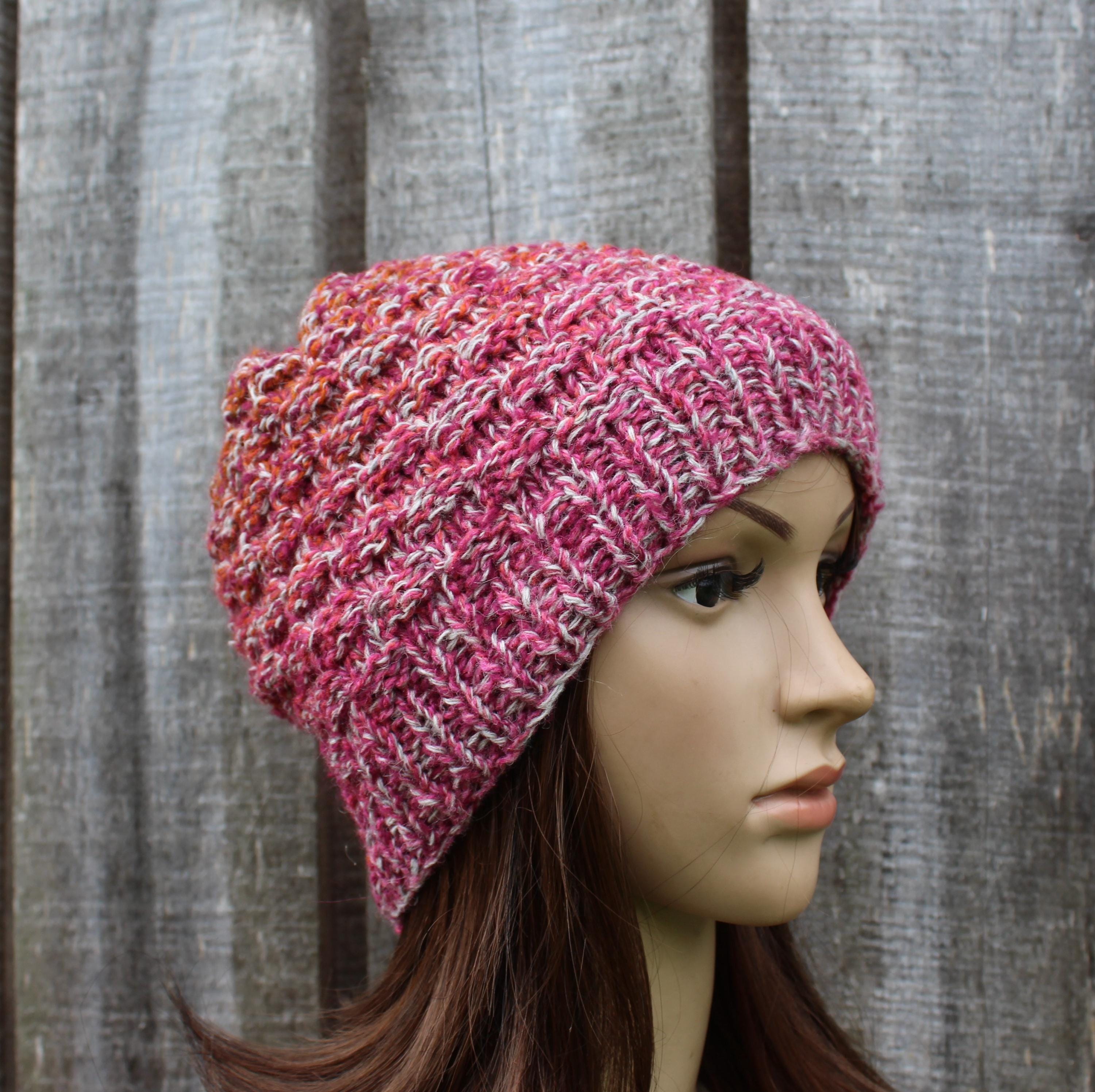 Mannequin head wearing a pink knitted beanie against a wooden panel background