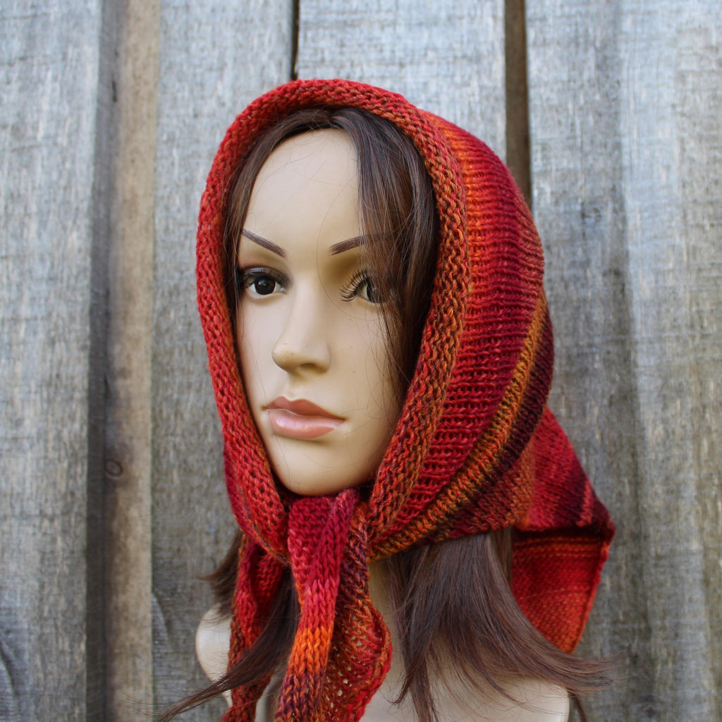 Mannequin head wearing a red and orange knitted kerchief against a wooden background