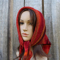 Mannequin head wearing a red and orange knitted kerchief against a wooden background